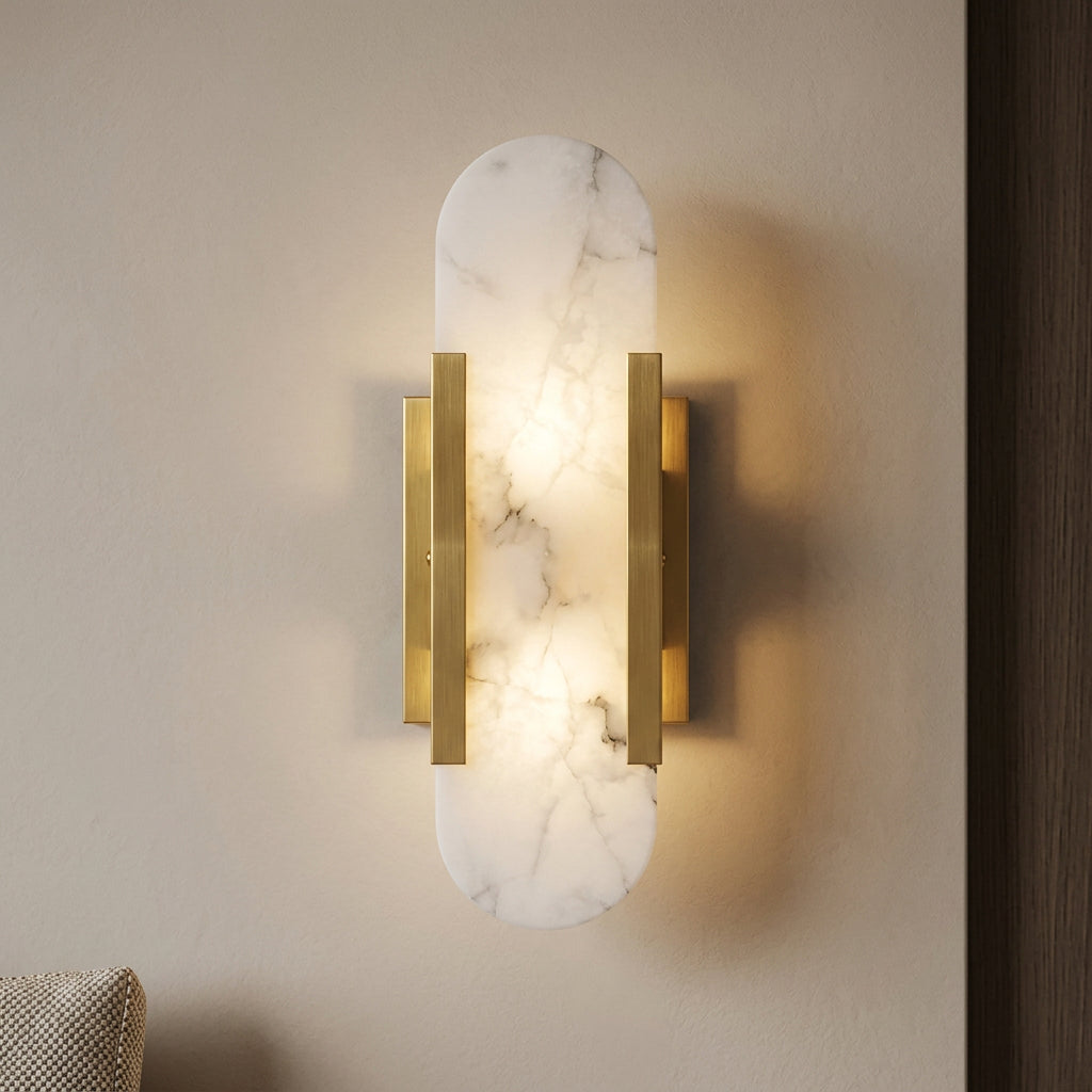 A modern wall-mounted sconce light fixture with a frosted white oval glass shade and brushed gold metal arms, shown lit against a gray wall.