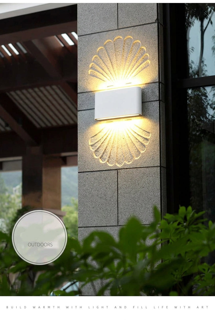 Outdoor wall light fixture on a building exterior with greenery in the foreground.