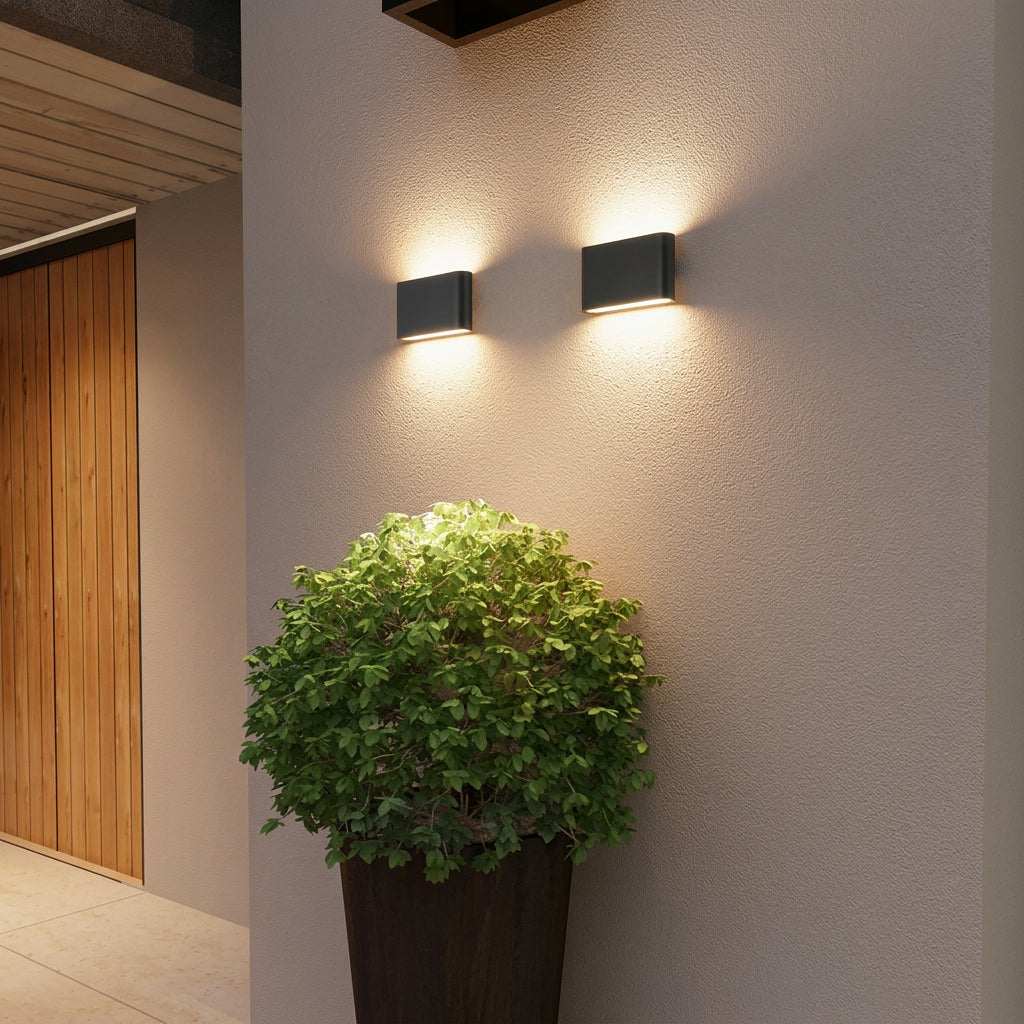 Two wall-mounted outdoor lights on a light gray wall with a potted plant in the foreground.
